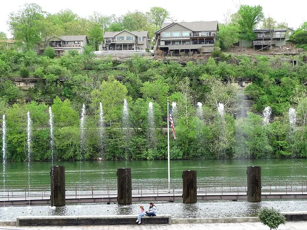 Homes on a green hillside above fountains on the White River in Branson