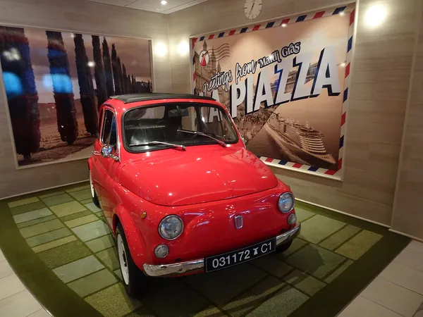 A red vintage Fiat under a Piazza sign on Mardi Gras