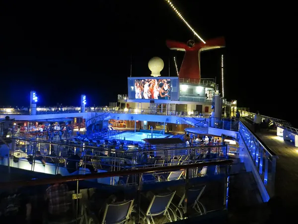 The Lido deck of Carnival Glory lit in blue at night, with the big screen glowing