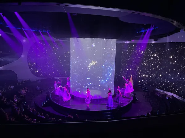 A show on the stage of the Theater aboard Celebrity Apex, lit in violet and blue