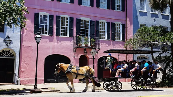 A horse-drawn carriage passing pink and blue historic houses in Charleston
