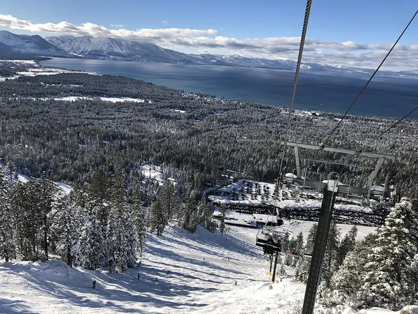Lake Tahoe below a snowy ski run and chairlift at Heavenly Mountain Resort