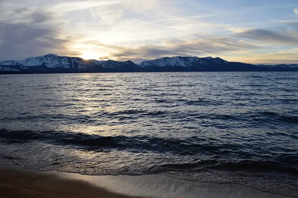 Winter sunset over the water and snowy mountains at Lakeside Beach, Lake Tahoe
