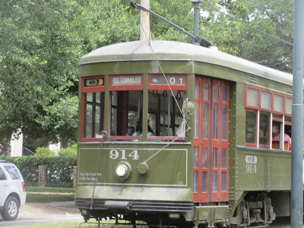 A green St. Charles Avenue streetcar passing under the trees in Uptown New Orleans
