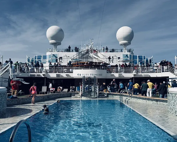 The sunny pool deck of Ruby Princess with loungers and a big blue pool under a blue sky