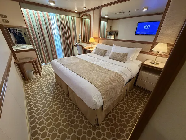 A balcony stateroom on Ruby Princess with its bed, TV and glass door to the balcony