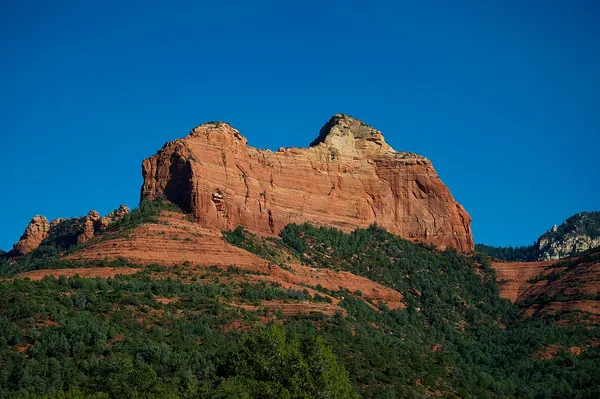 A red rock butte rising above green desert under a deep blue sky in Sedona