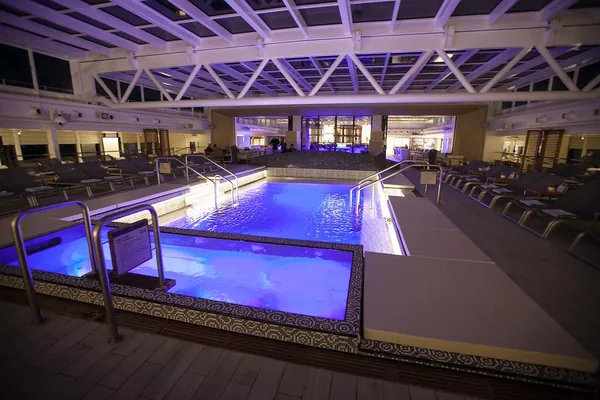 The Main Pool under its retractable glass roof, lit blue in the evening, on Viking Star