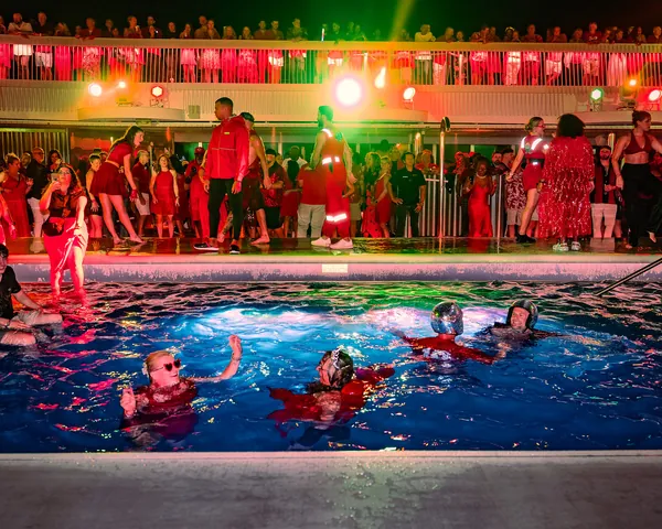 Performers in the pool under red and green lights during Scarlet Night on Valiant Lady