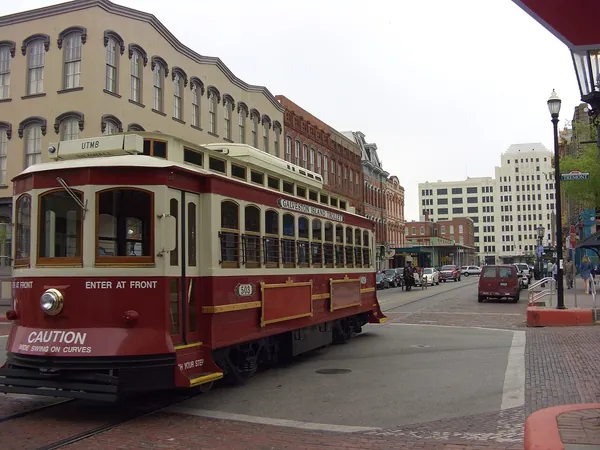 A red Galveston Island Trolley on The Strand, lined with Victorian brick buildings