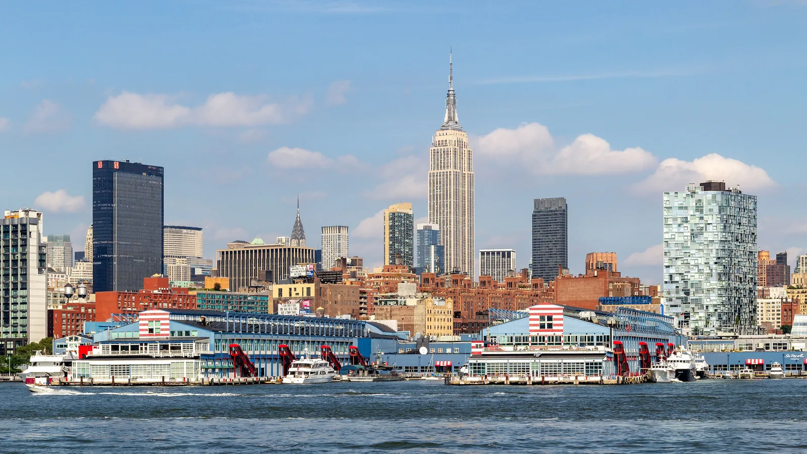 The Manhattan skyline with the Empire State Building under a bright blue sky, seen across the Hudson River