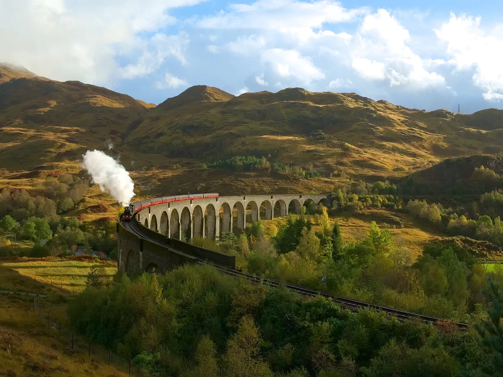 Steam train crossing the curved Glenfinnan Viaduct through green Scottish Highland hills