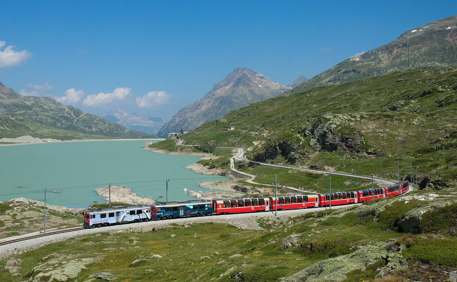 Red Bernina Express train beside the turquoise Lago Bianco in the Swiss Alps