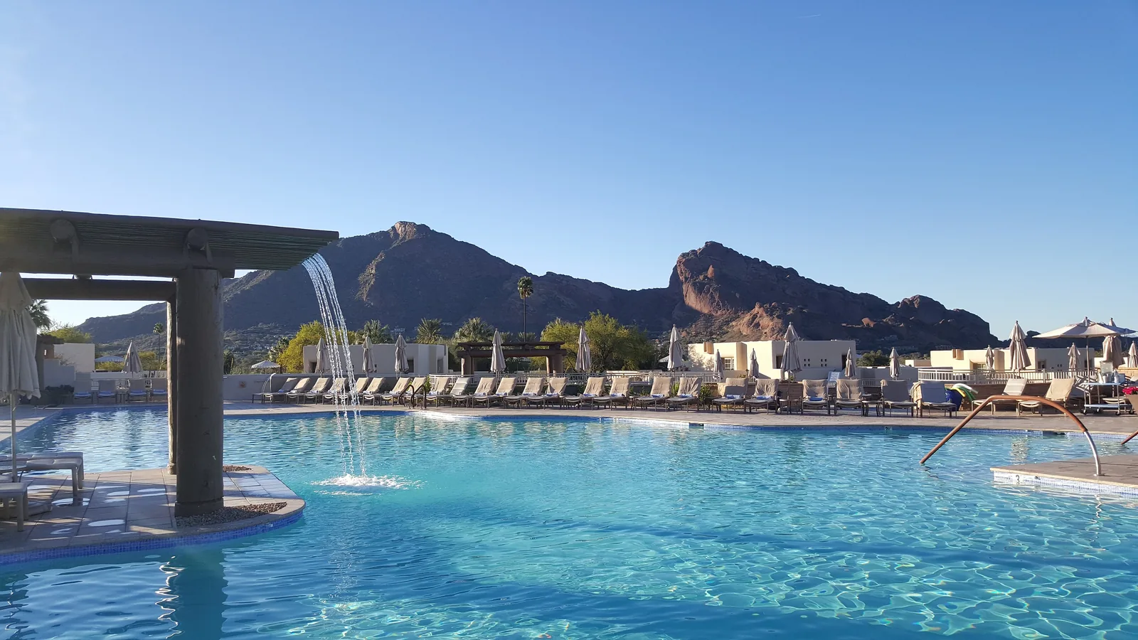 Resort swimming pool with palm trees and Camelback Mountain under a blue sky in Scottsdale, Arizona